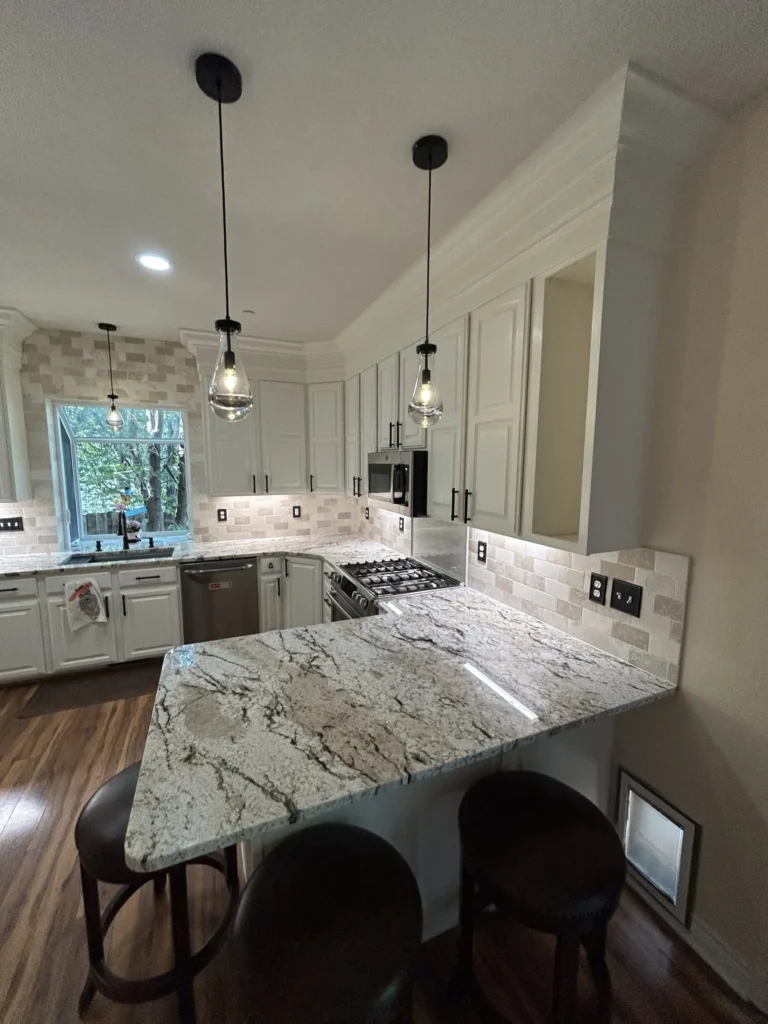 Remodeled kitchen with a granite peninsula, bar stools, white cabinets and pendant lights