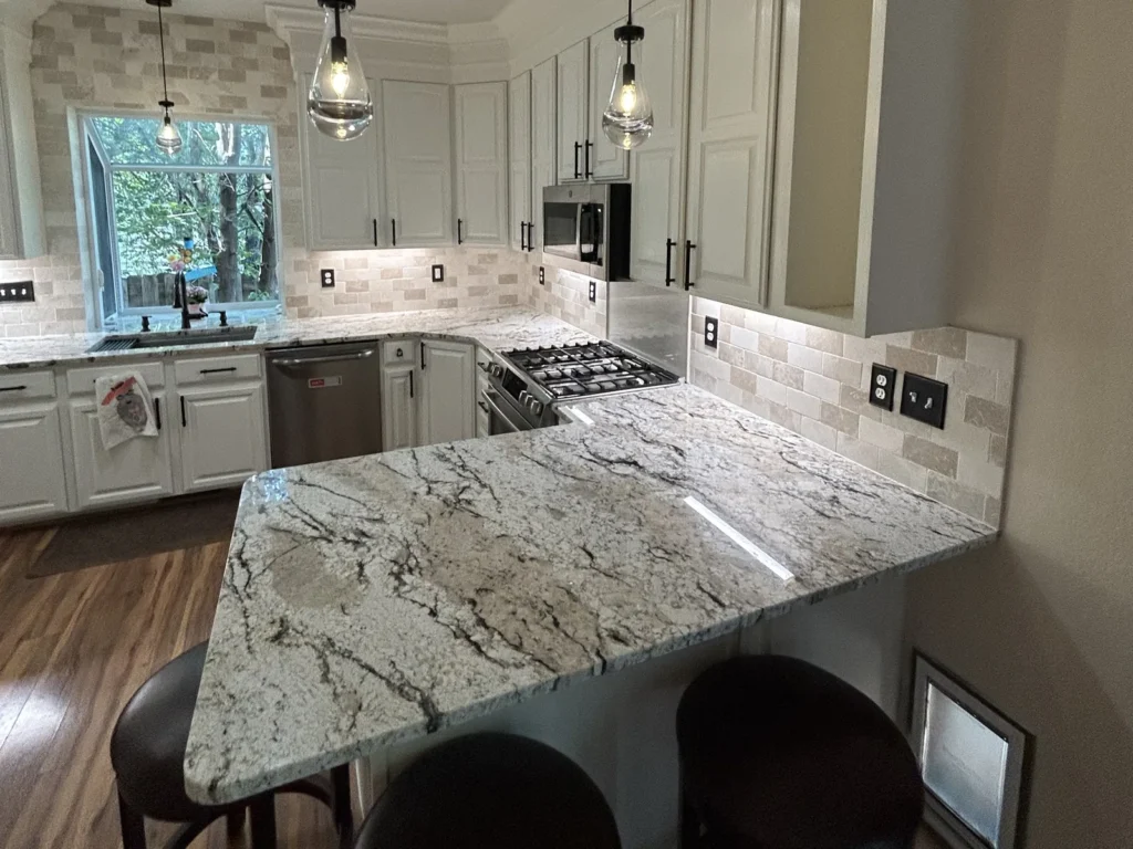 Remodeled kitchen with a granite peninsula, bar stools, white cabinets and pendant lights