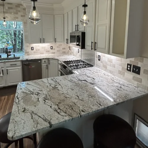 Remodeled kitchen with a granite peninsula, bar stools, white cabinets and pendant lights