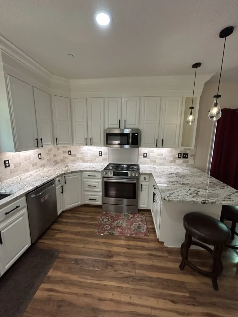 White kitchen cabinets with crown molding, granite counters, stainless range and microwave, and tile backsplash