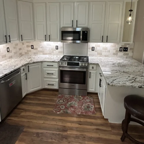 White kitchen cabinets with crown molding, granite counters, stainless range and microwave, and tile backsplash