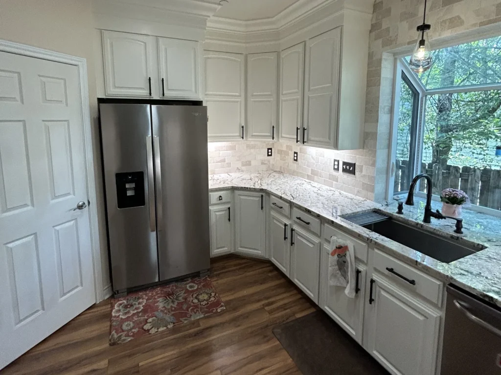 Remodeled kitchen with white cabinets, stainless refrigerator, undermount sink and window over the counter