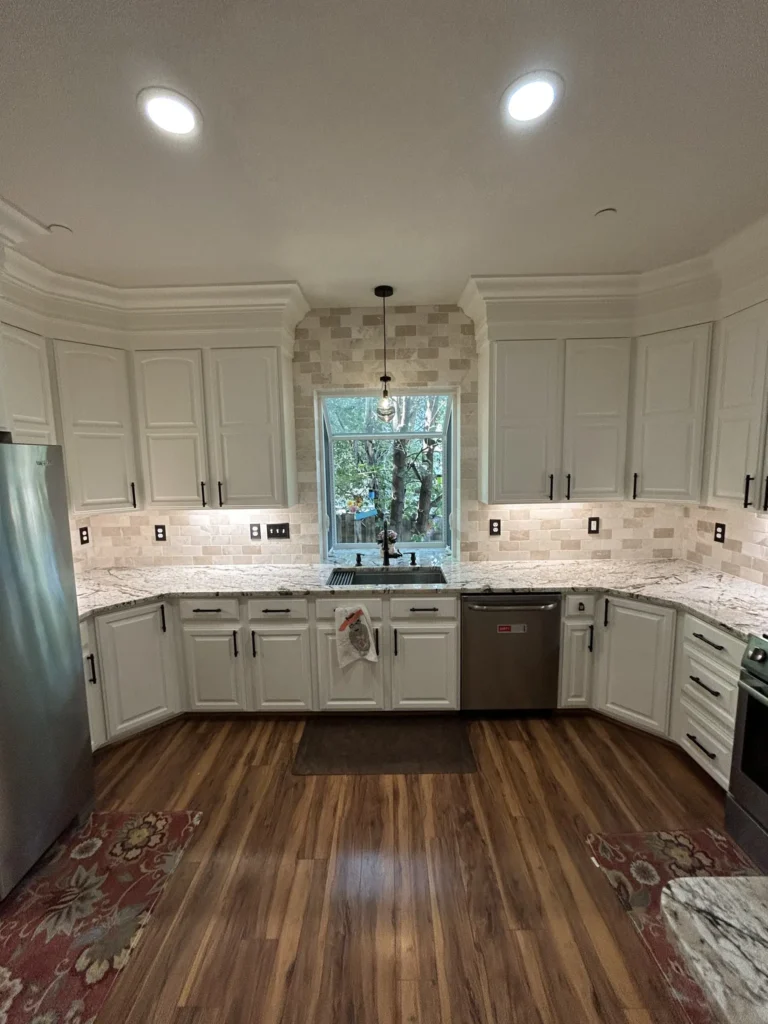 U-shaped kitchen remodel with white cabinets, stone tile backsplash, garden window and wood-look floors