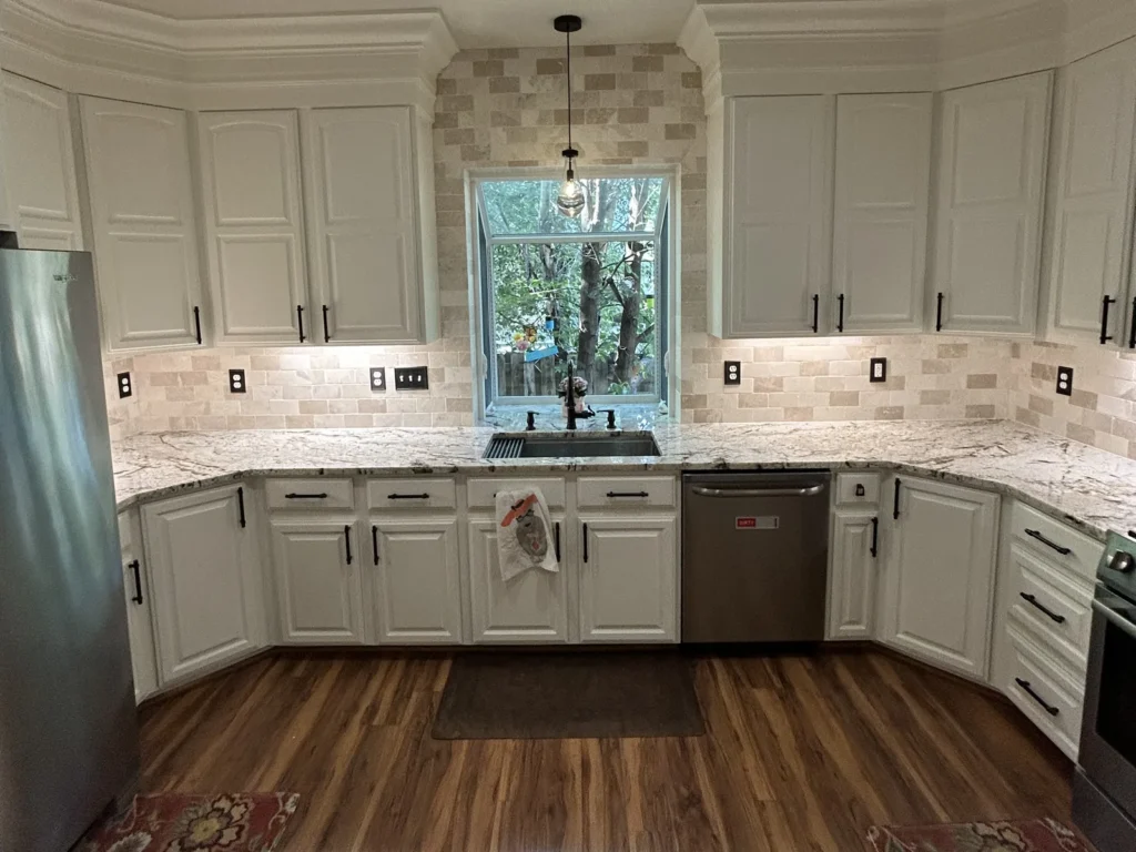 U-shaped kitchen remodel with white cabinets, stone tile backsplash, garden window and wood-look floors