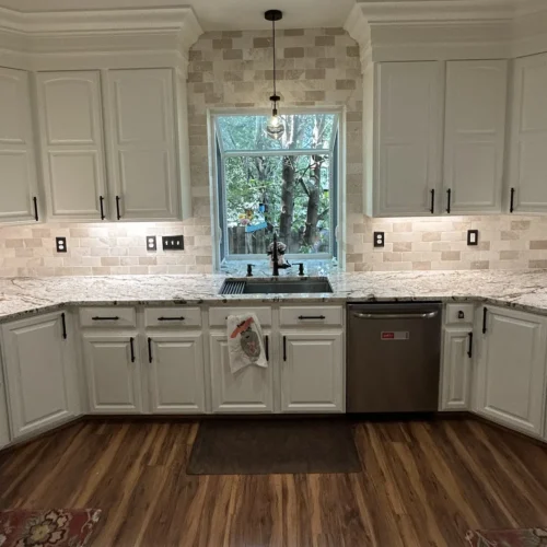 U-shaped kitchen remodel with white cabinets, stone tile backsplash, garden window and wood-look floors